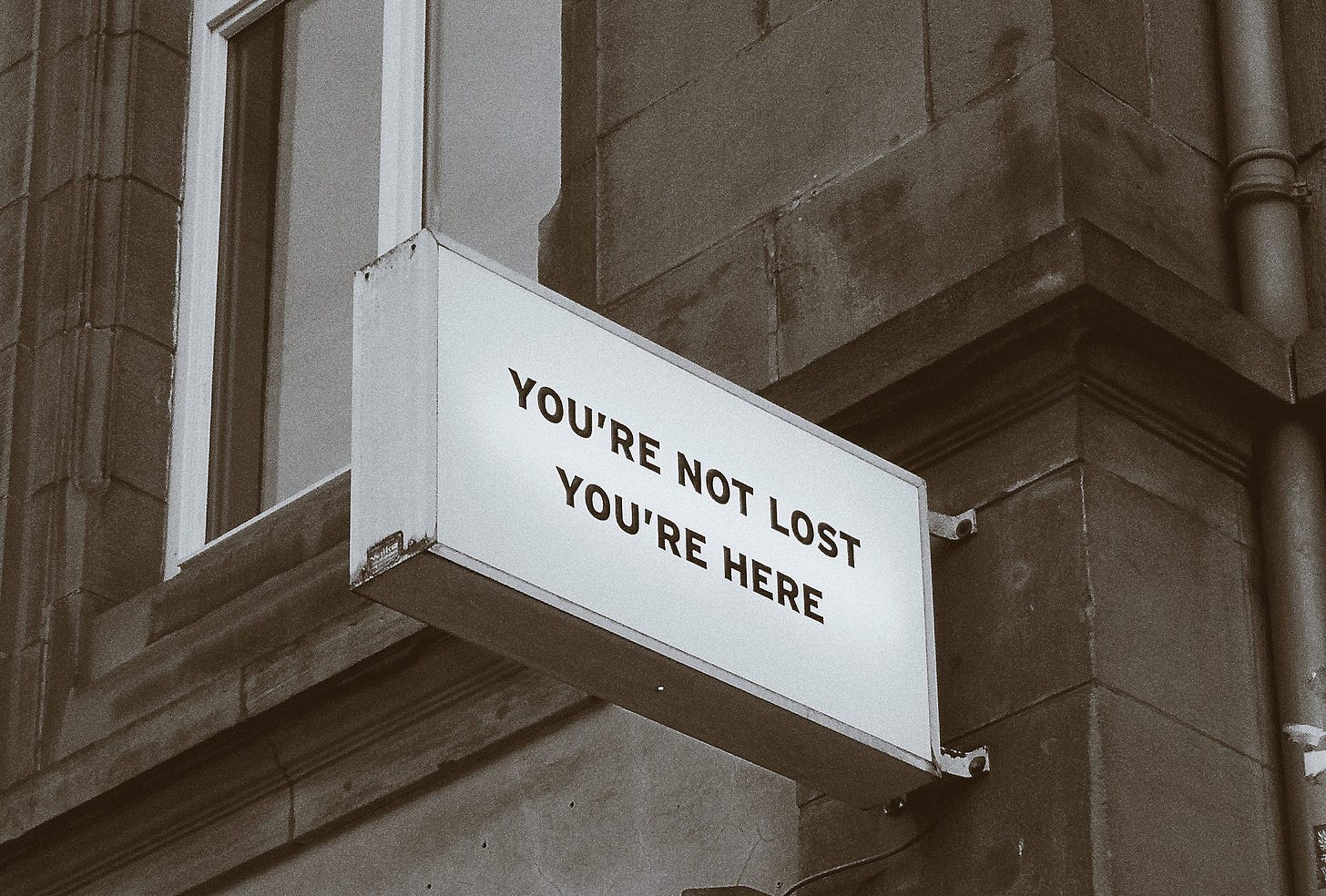 Fachada de um prédio antigo que contém uma placa com os dizeres: you’re not lost. you’re here. Em português: você não está perdido. você está aqui.