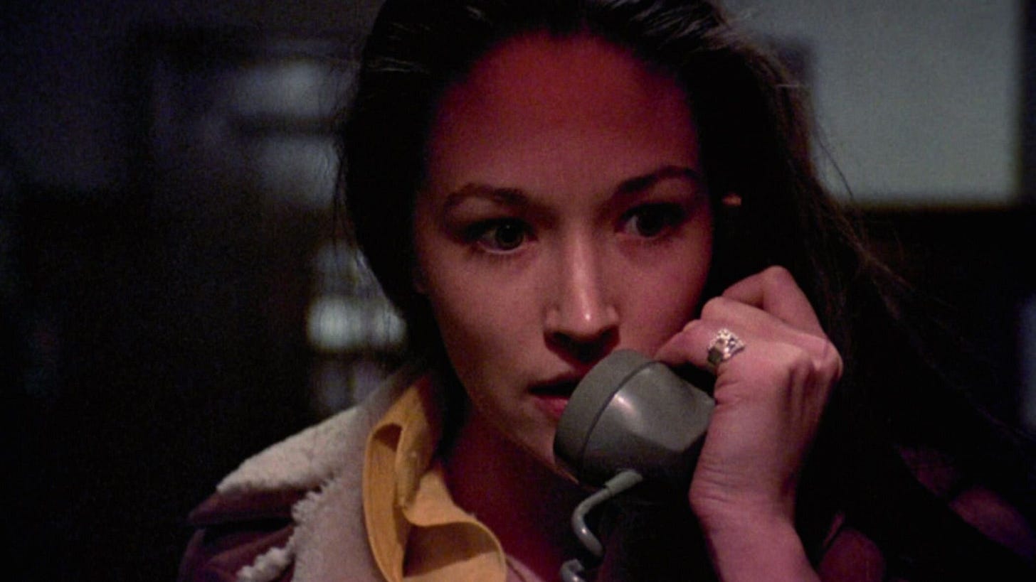 A young woman holding a vintage telephone to her ear, looking concerned and focused, with a dimly lit background adding a suspenseful atmosphere. This is a still from the 1974 horror film Black Christmas.