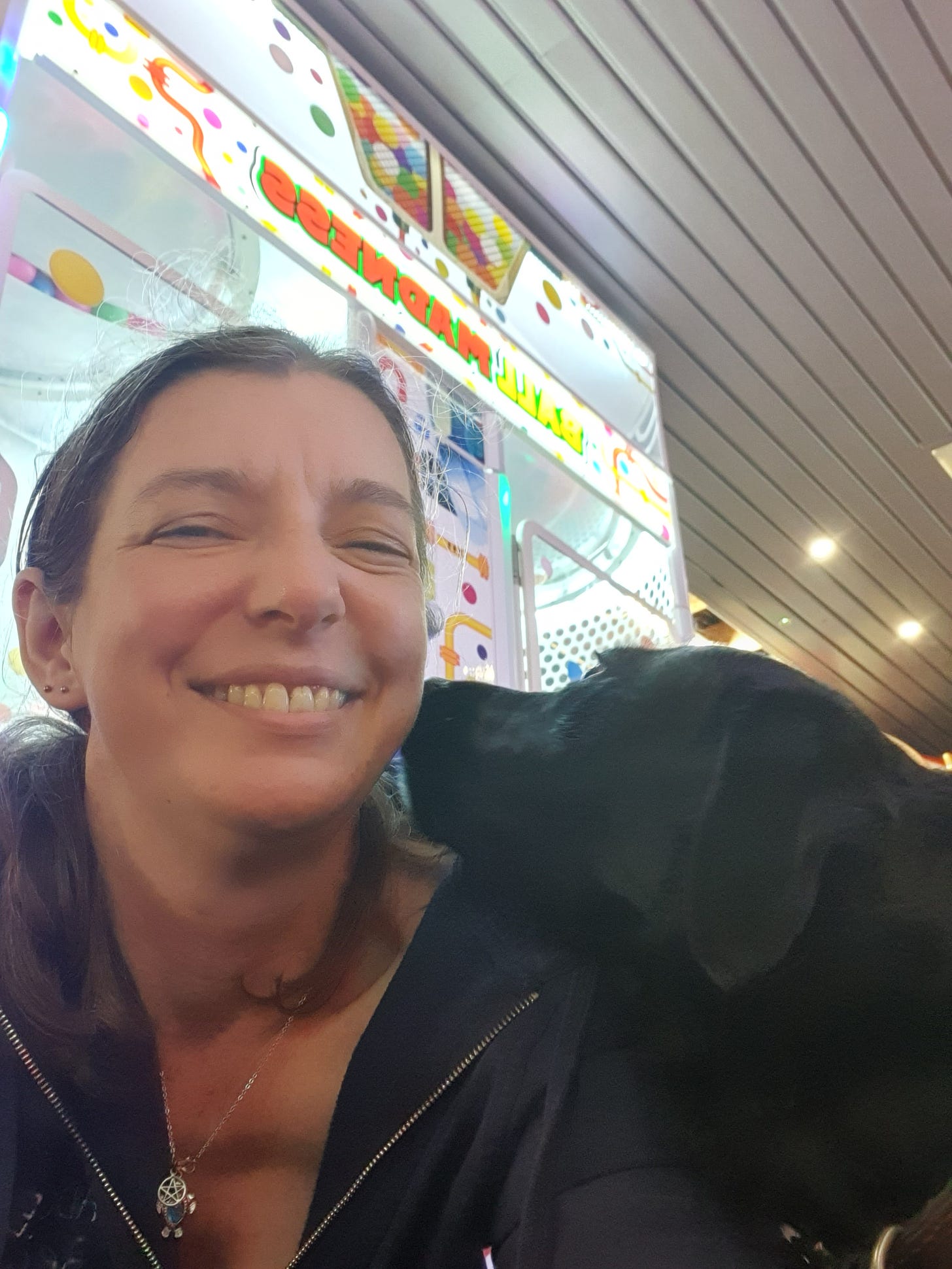 A happy smiling woman and her black dog, who is giving her kisses