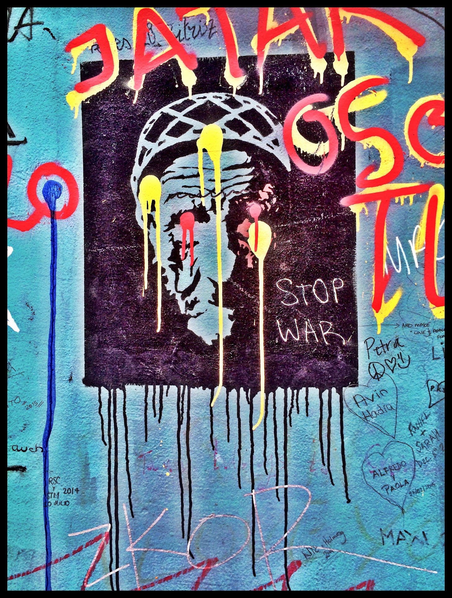 A spray painted image of a face on a wall, with lots of graffiti on top and around it, including the words "STOP WAR."