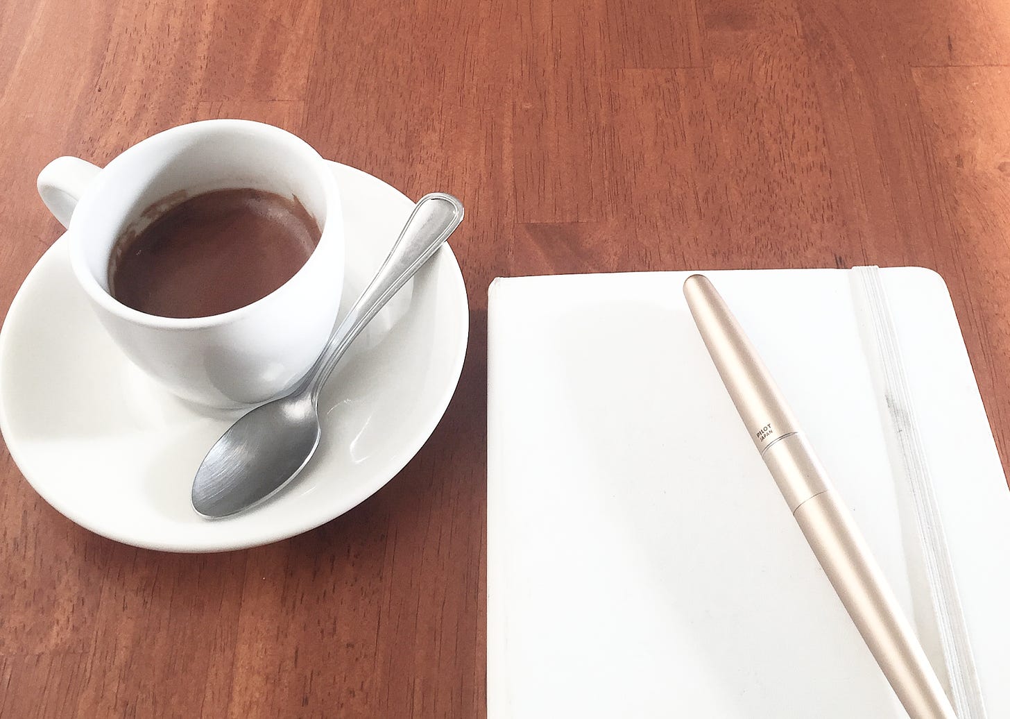 A shot of espresso with a white notebook and gold pen, ready to start writing morning pages