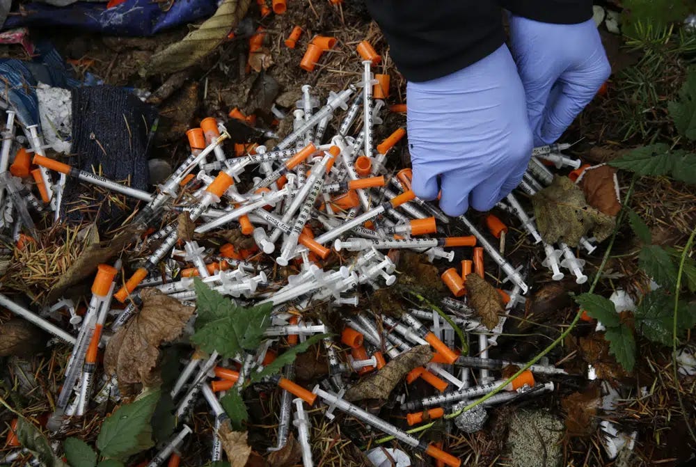 FILE - A volunteer cleans up needles used for drug injection that were found at a homeless encampment in Everett, Wash., Nov. 8, 2017. A temporary law that makes possession of small amounts of drugs a misdemeanor expires on July 1, so if lawmakers fail to pass a bill, Washington would become the second state — after neighboring Oregon — to decriminalize drug possession. Lawmakers said Tuesday, May 2, 2023, they were increasingly optimistic a compromise will be reached to avoid those consequences. (AP Photo/Ted S. Warren, File)