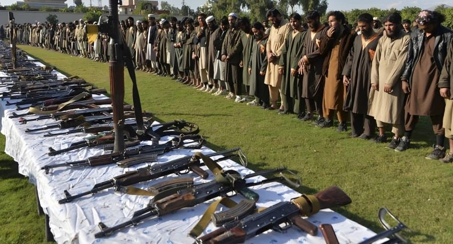 Hundreds of Jihadists lined up, displaying an array of weapons laid out in front of them on the ground, ready for mobilization.