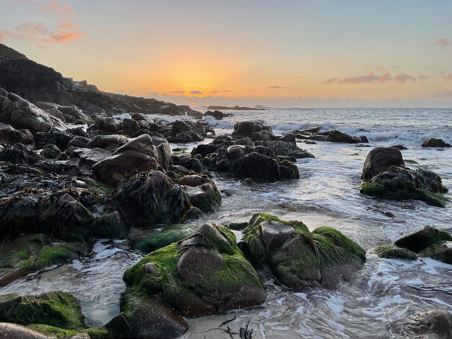 close up of rocks at the sea edge with the sun setting in the background