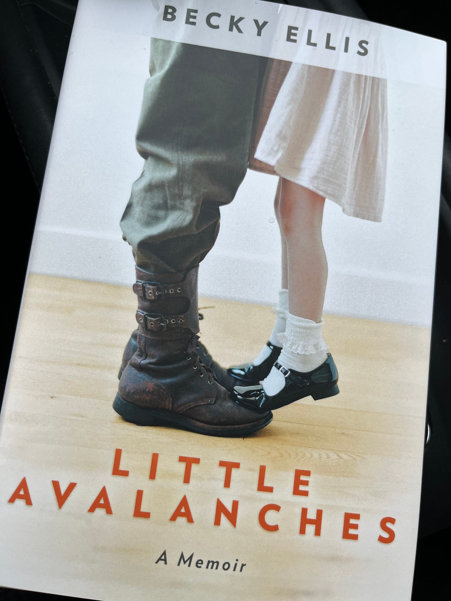 Image of two people from knee down  Man in military pants/boots. Child in dress, short socks and patent leather Mary Jane style shoes and title of memoir Little Avalances by Becky Ellis 