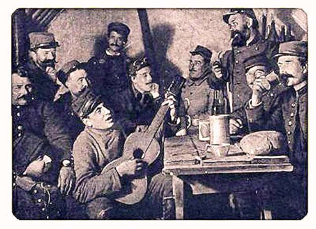 A grainy photo of group of French soldiers sat around a table singing and drinking. One is playing a guitar. The original caption, before I got my hands on it, reads “Le soir, dans l'abri de la tranché, vin et musique.“