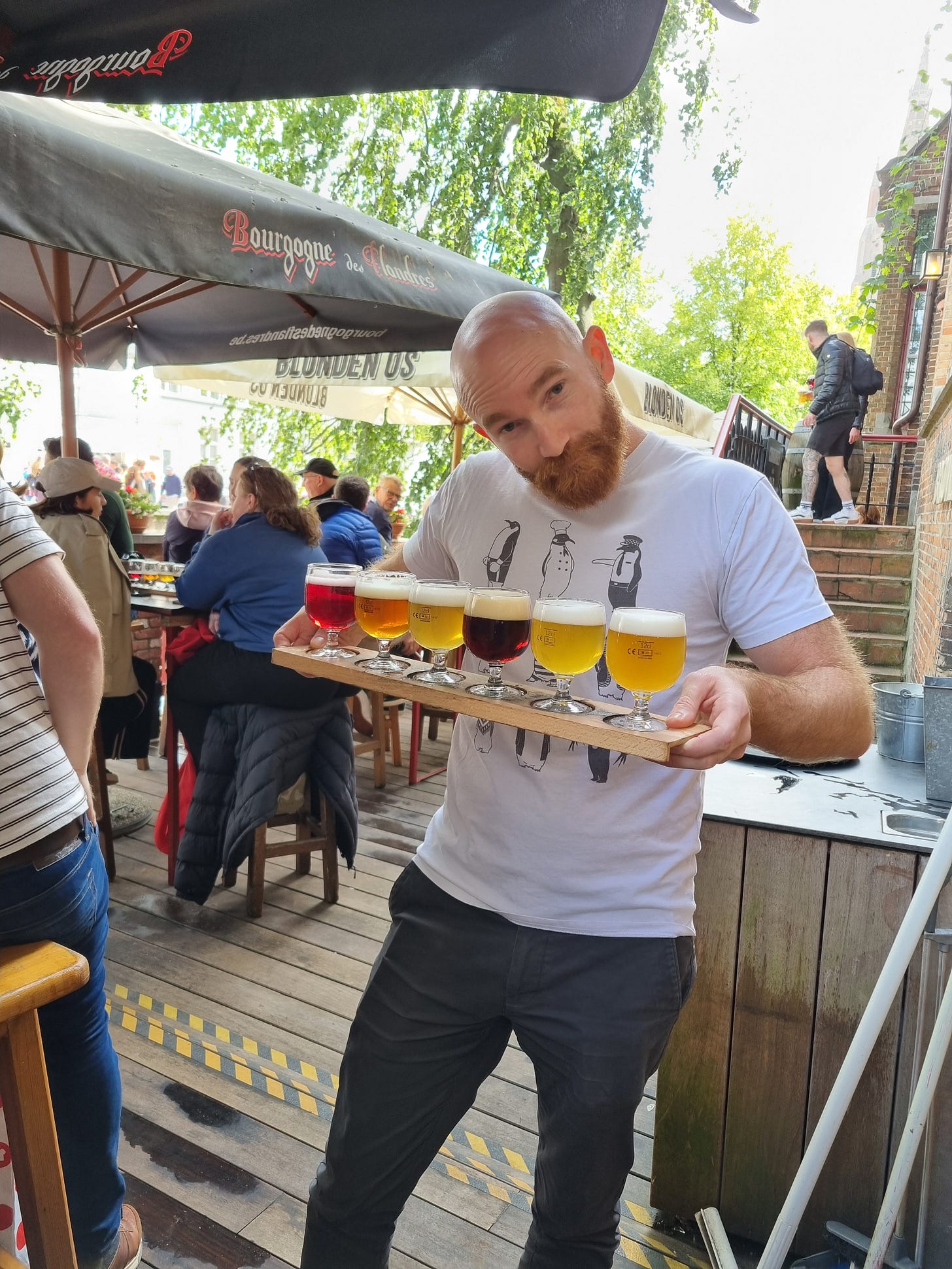 Photo of Dave carrying a tasting paddle of beers and wearing a shirt with penguins on it.