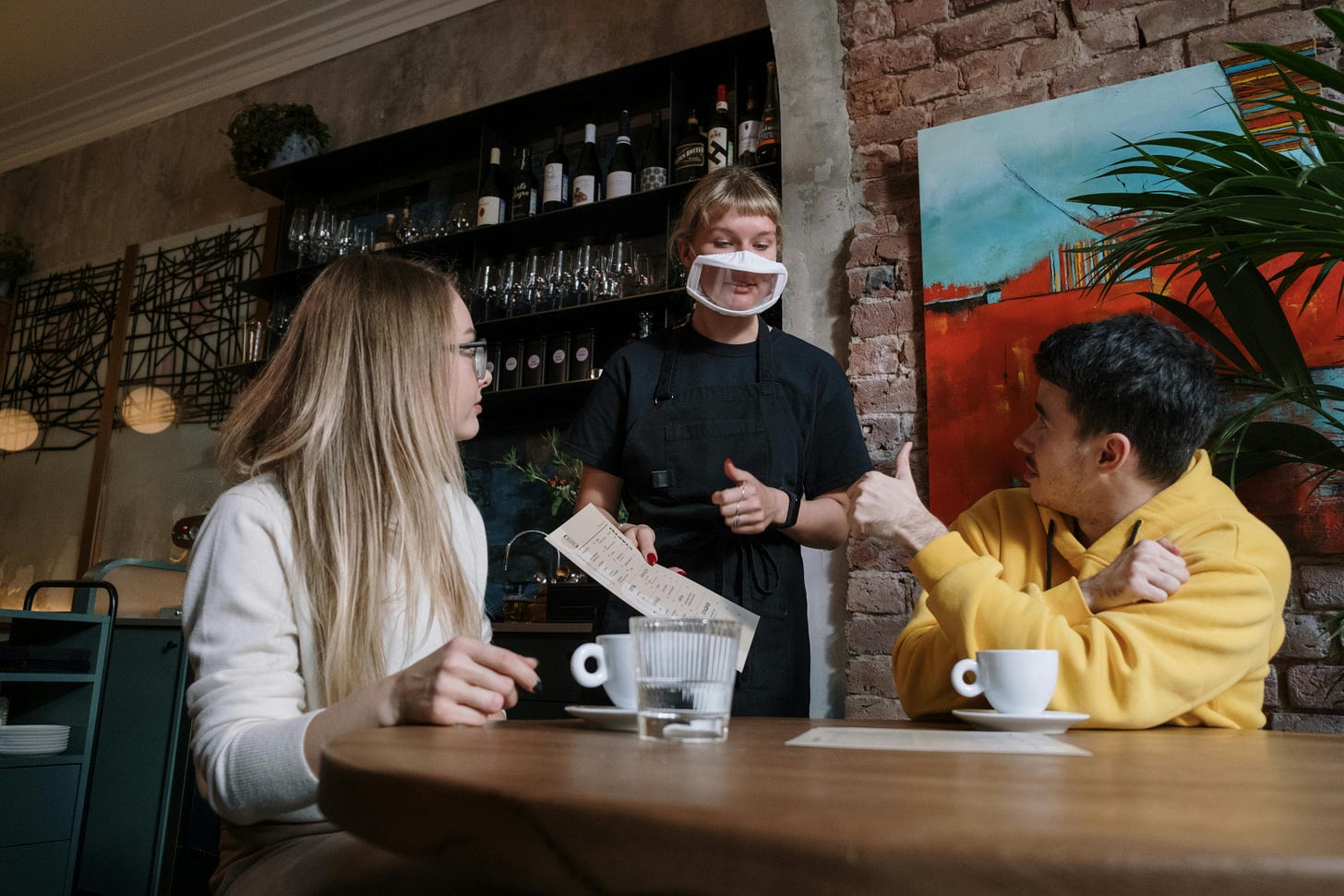 Waitress with see thru mask hands menu to customers Waitress with see thru mask hands menu to customers