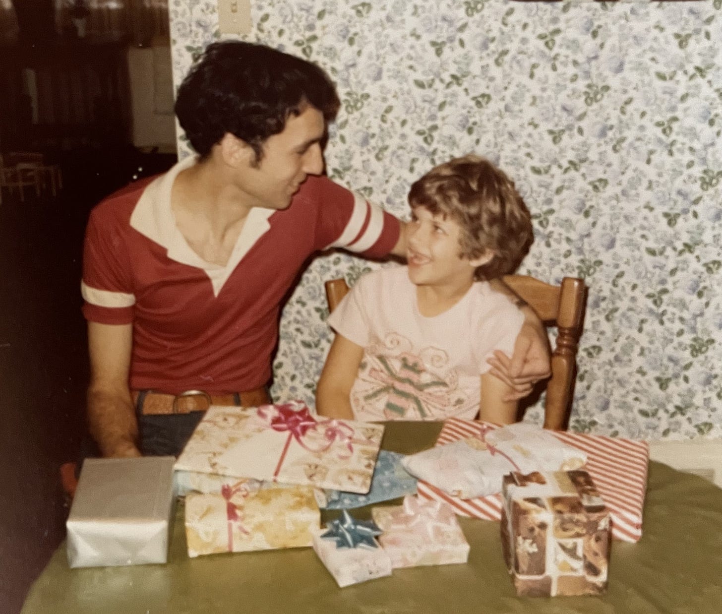 A young man and girl smile at each other behind a pile of wrapped gifts