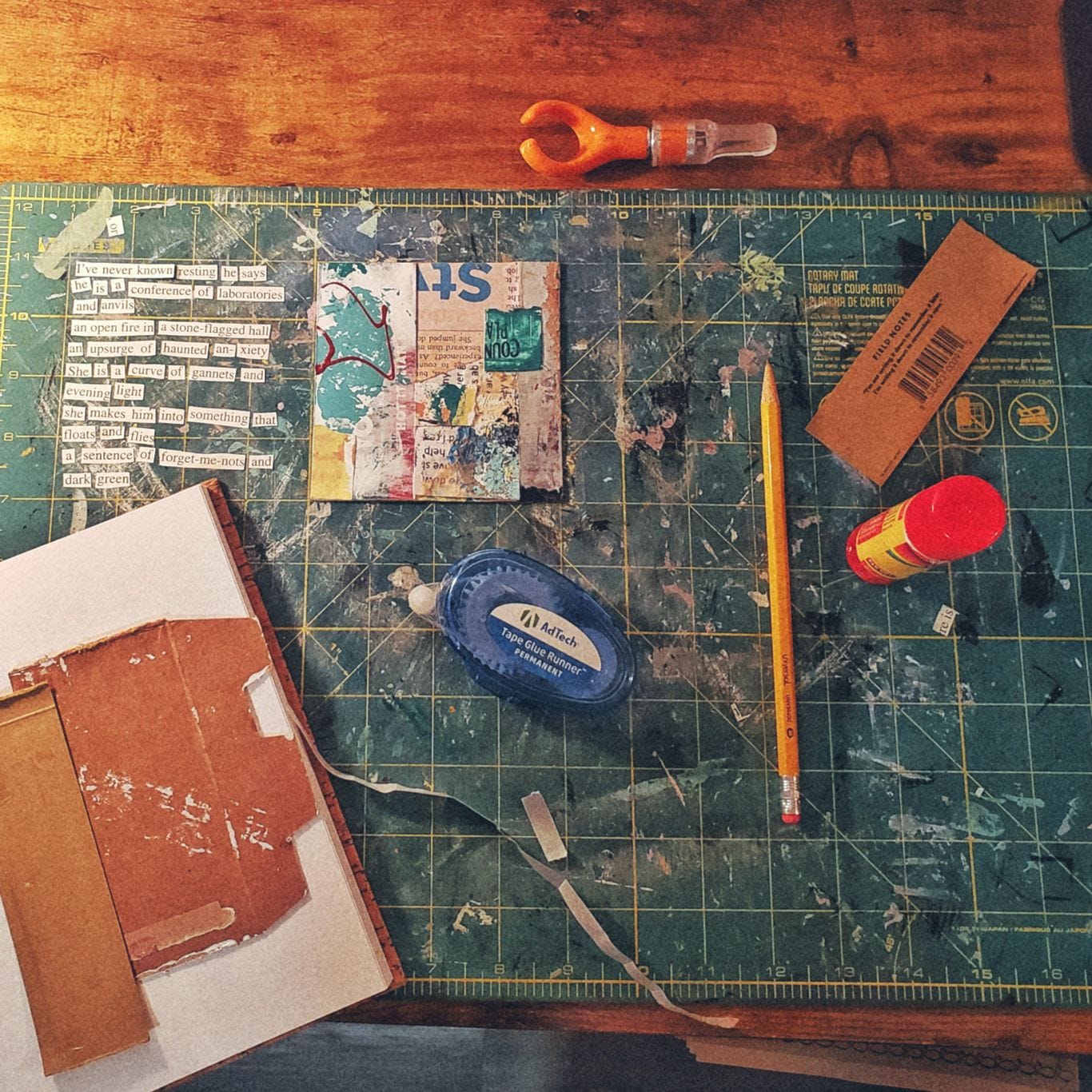 various art supplies and collage materials scattered on a desk with a green cutting mat