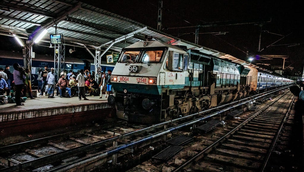 a train arrives at a station in India at night. There are many people on the platform