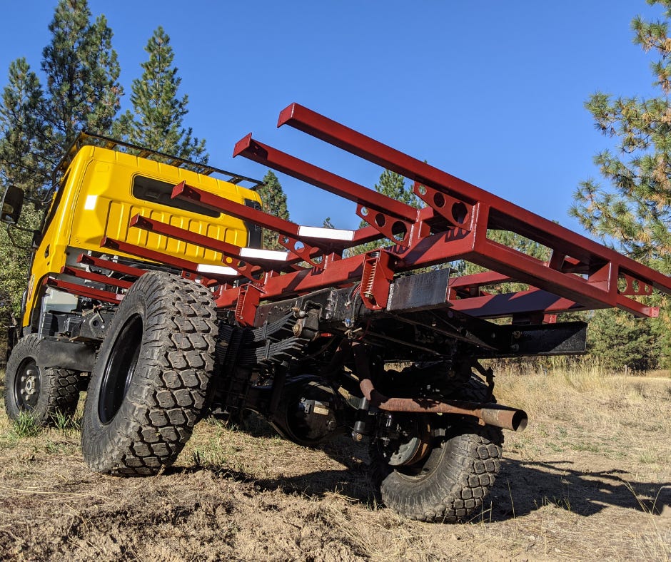 yellow truck with red subframe, set against green pine trees and a blue sky