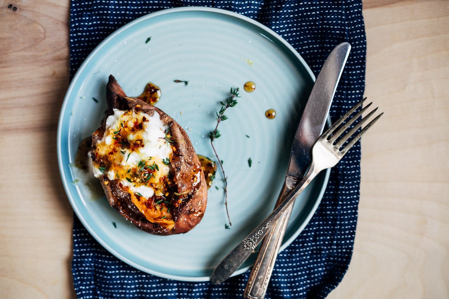 A plate with a roasted sweet potato topped with herbs and ricotta. 