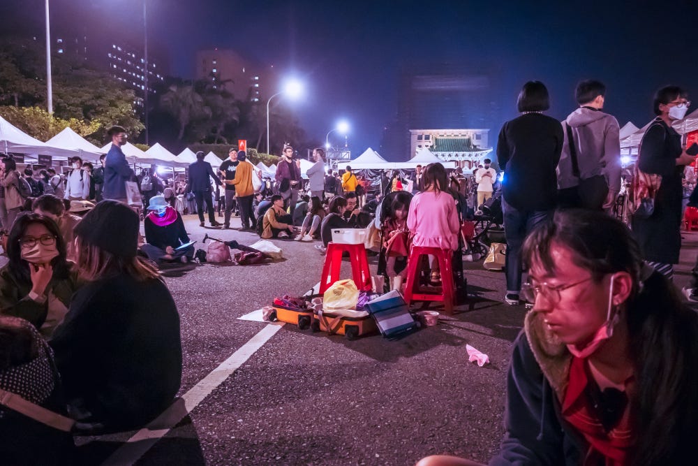 A young girl in a pink jacket sits on a red stool surrounded by other attendees of the 2023 Gongsheng Music Festival 