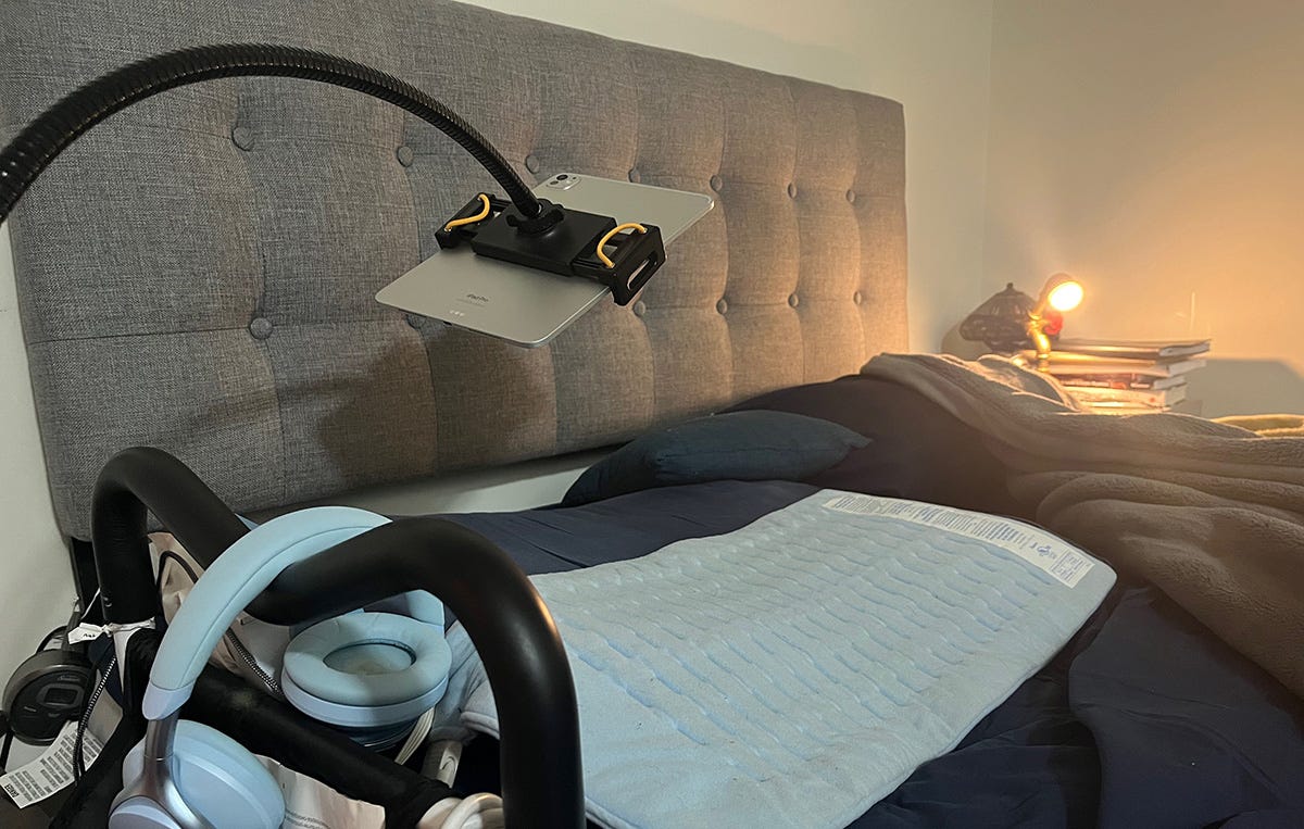 Queen sized bed with blue sheets and a grey padded headboard. An iPad stand arches over the bed so that someone who is lying in the bed can work on the iPad suspended overhead.