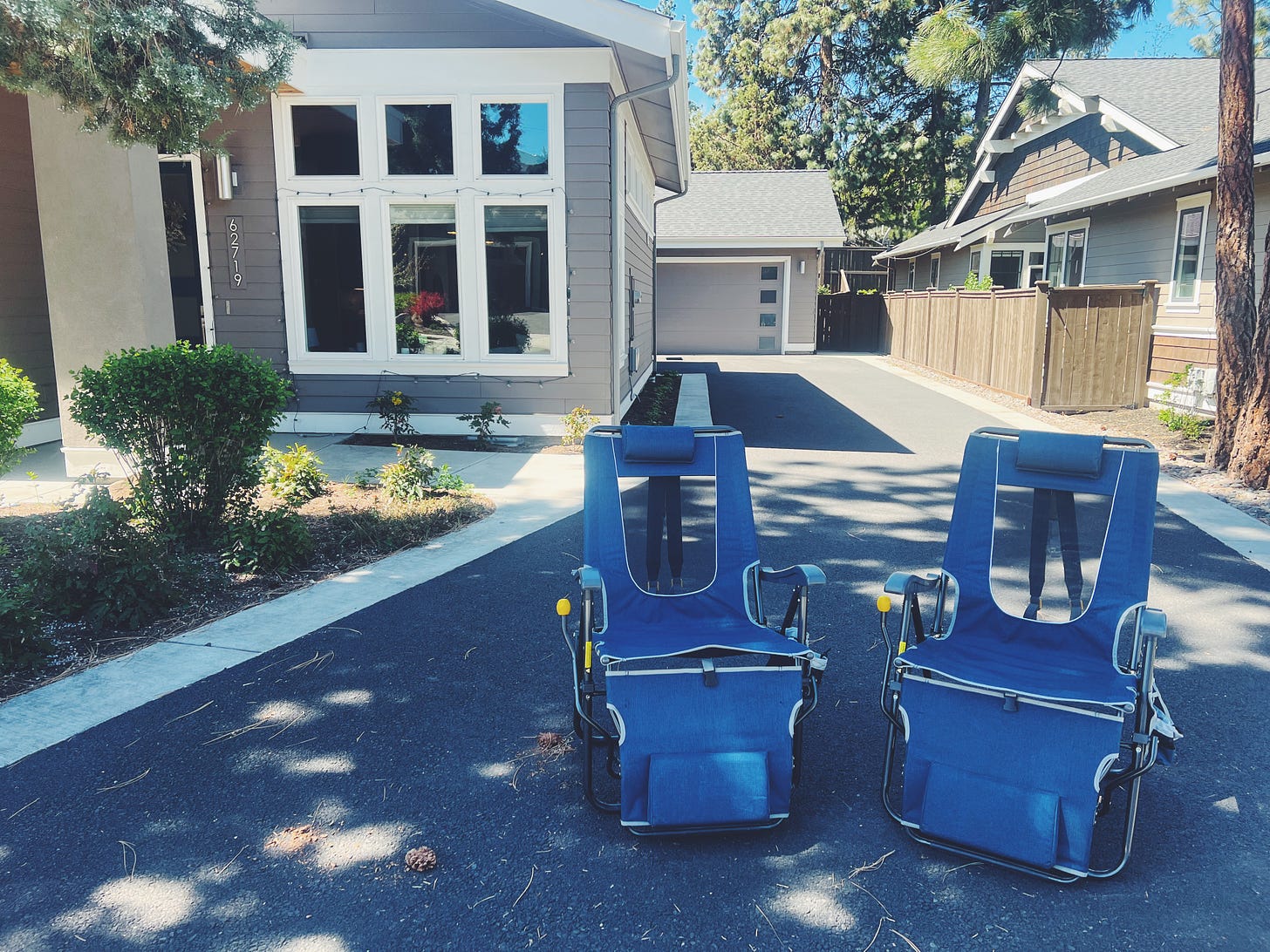 Two lawn chairs in the driveway of a home, facing out to the street