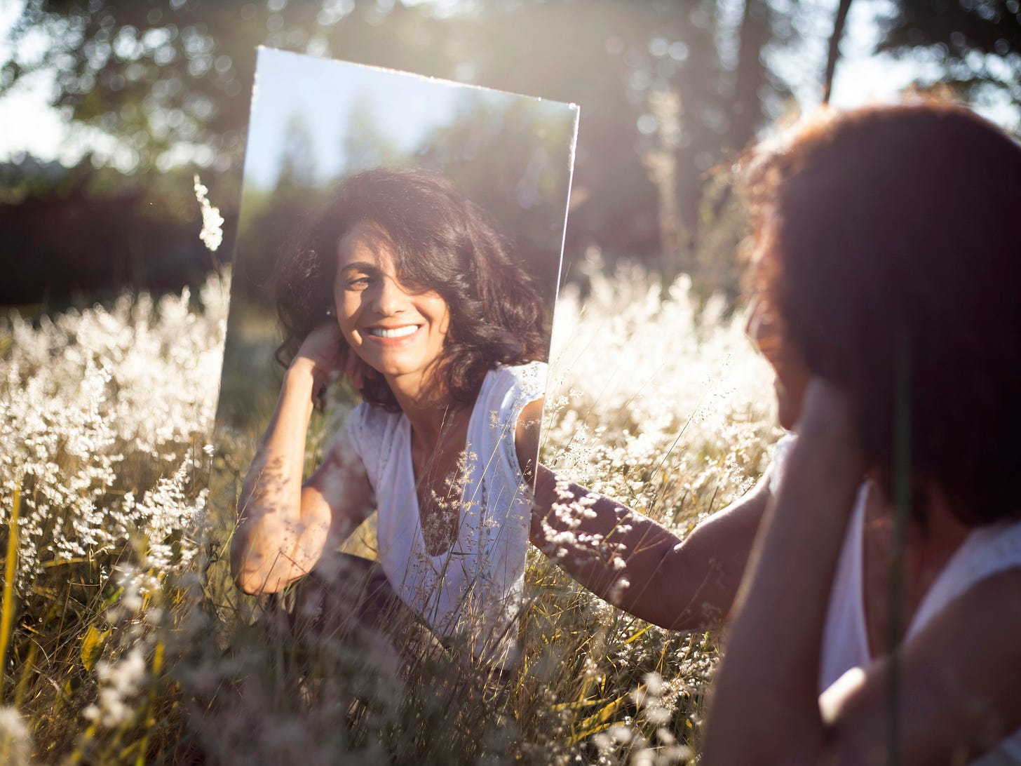 a woman in a summer meadow looking into a mirror