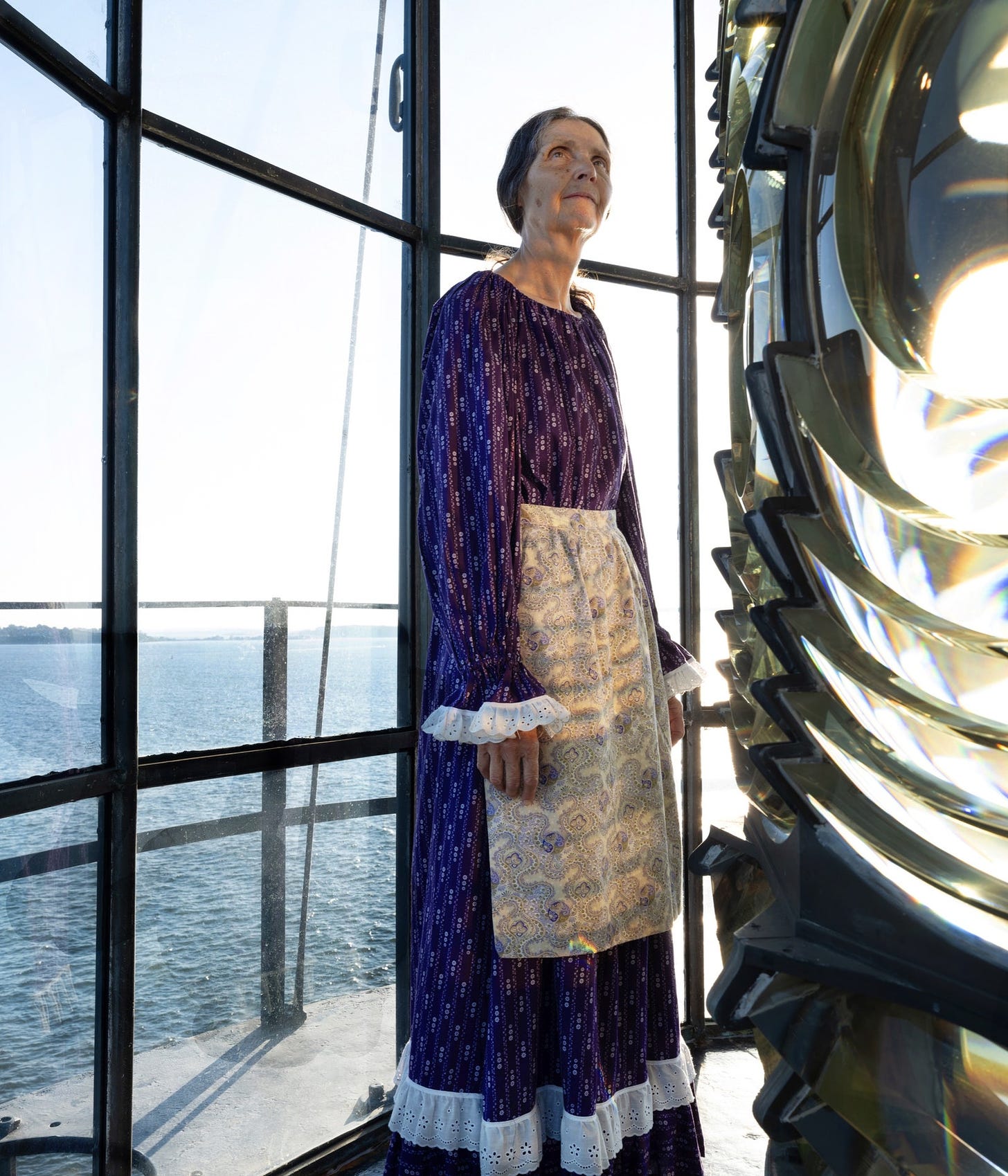 Sally Snowman standing by the Fresnel lens of Boston Light.