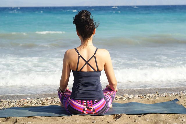 woman sitting on beach looking at ocean and meditation