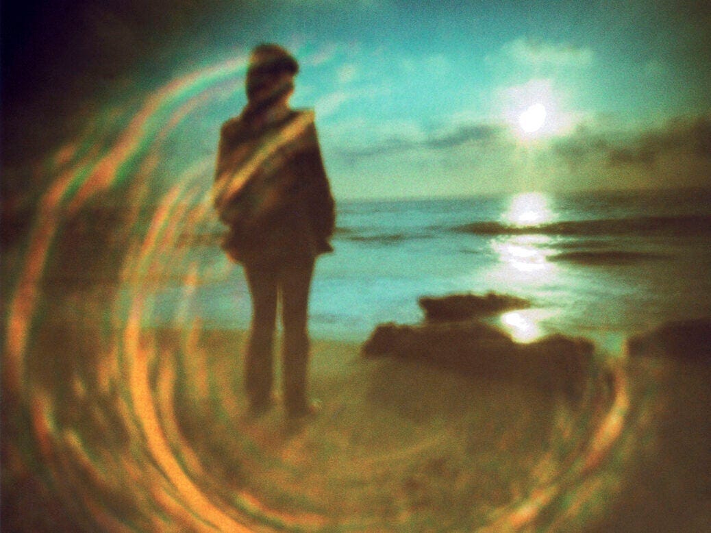 Photo shows silhouetted figure watching the sunset on. a beach with circular streaks of light