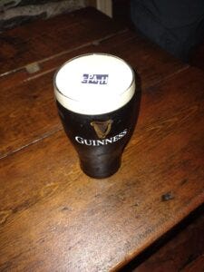 Image of a pink of Guiness beer with an edable tag that says EPATH floating on top. The beer is dark brown in color and there is about an inch of which foam on top.