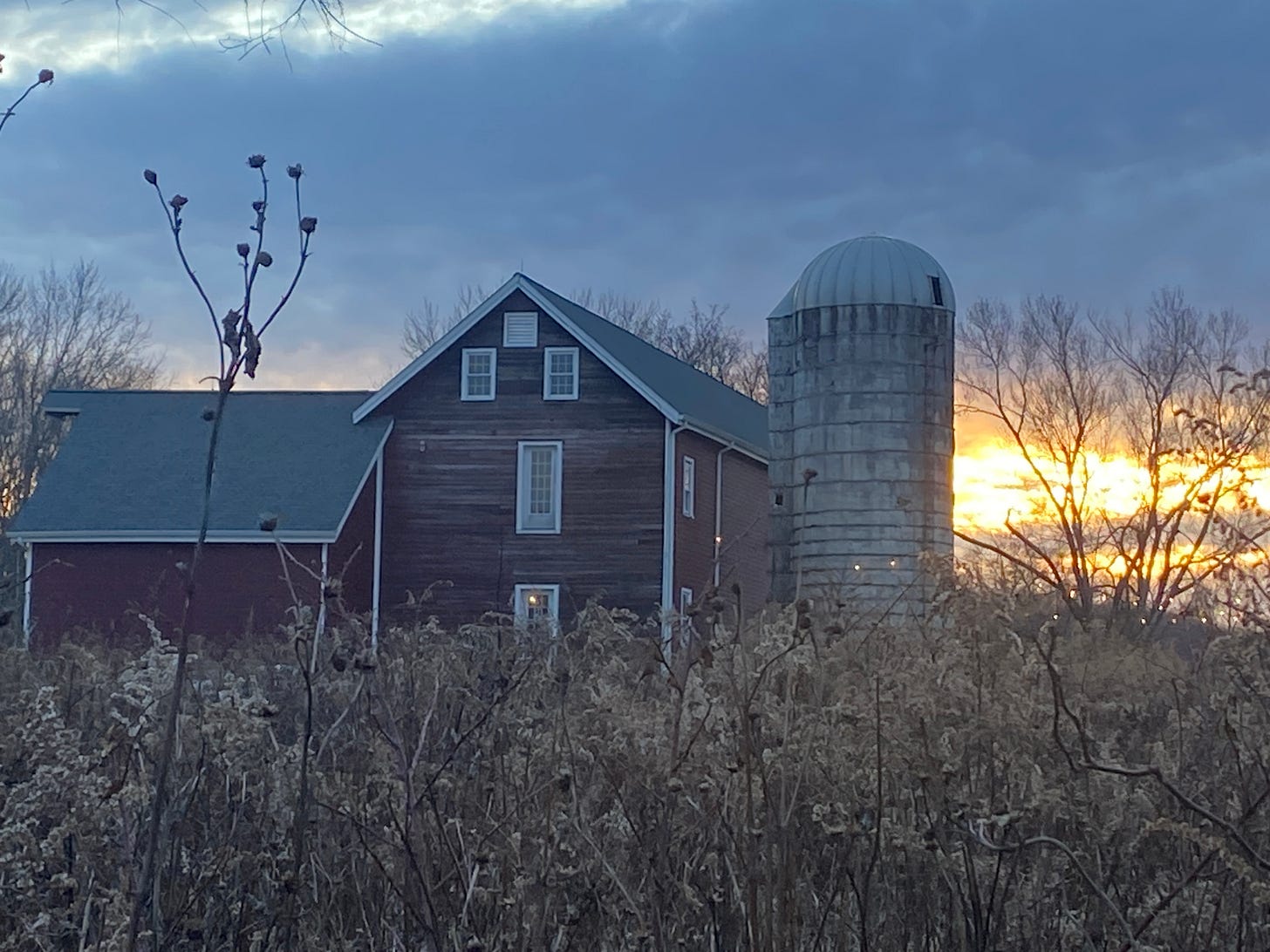 a red farmhouse. the sky behind is blue with a golden setting sun