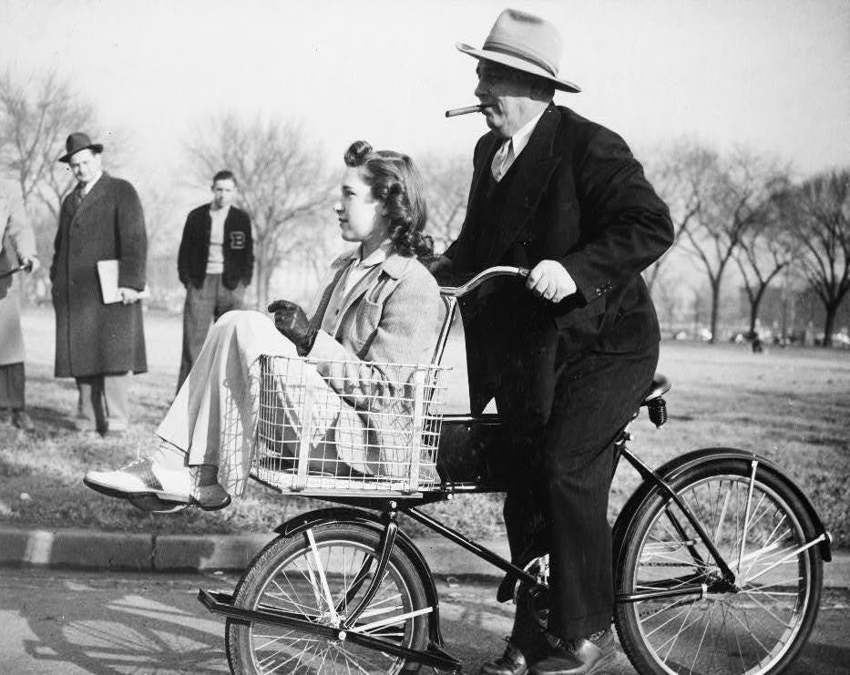 Leon Henderson, administrator of the wartime Office of Price Administration, pedals a Victory Bike... [+] in Washington, DC, 1942. Betty Barrett, an OPM stenographer, rides in the parcel basket.