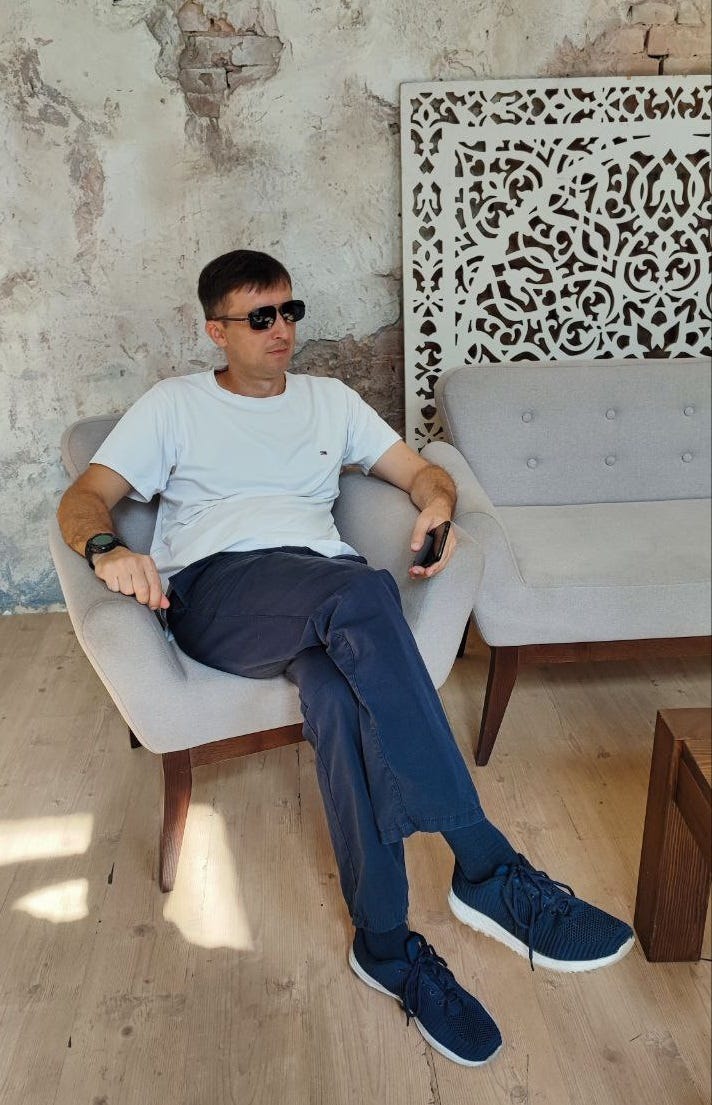A man in sunglasses sits in t-shirt and jeans holding a phone.