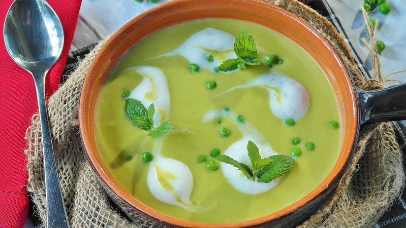 Pea soup in a bowl on a hessian sack. There are sprigs of mint & whole peas in the puréed soup
