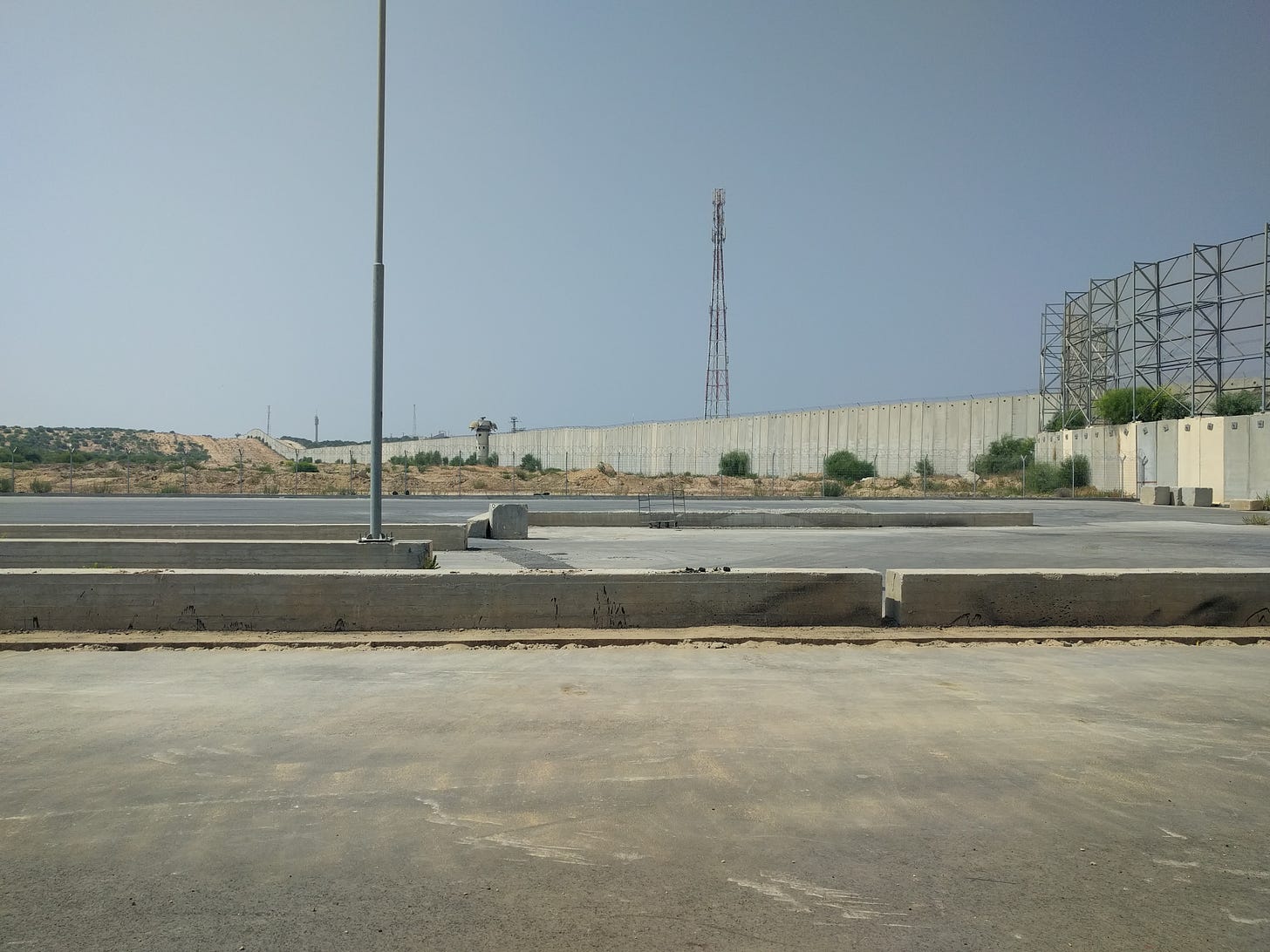 A large concrete wall topped with guard towers extends into the horizon under a blue sky