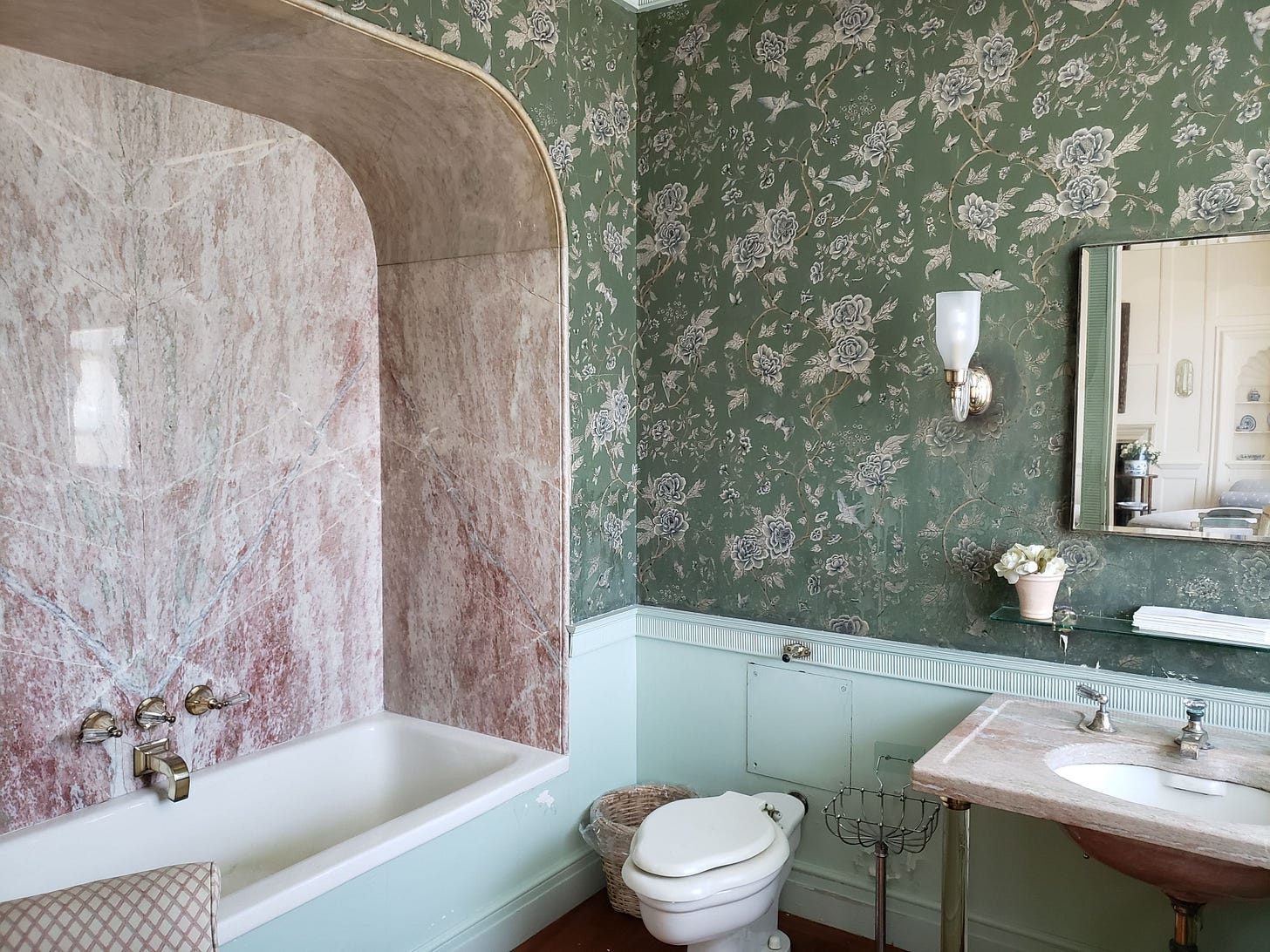 Bathroom with green floral wallpaper and a pink marble bath surround.