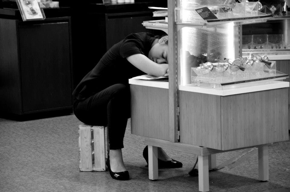 A shop worker sitting on a crate and napping over a low cabinet
