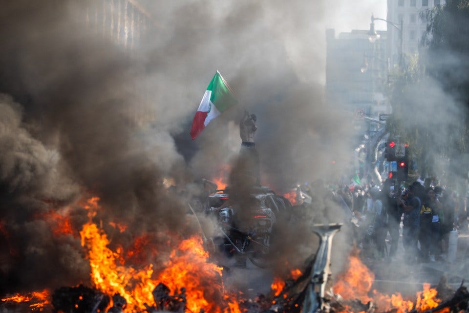 A man holds a Mexican flag atop a burning car during a protest in Los Angeles.