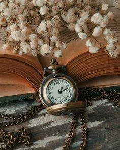 This may contain: an open book with a pocket watch sitting on top of it next to some flowers