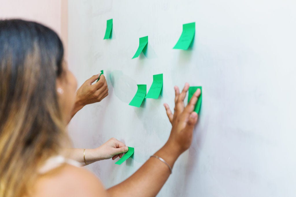 Alcune studenti di varie etnie, di cui vediamo solo le mani e un volto sfuocato, attaccano dei post it verdi a una lavagna bianca.