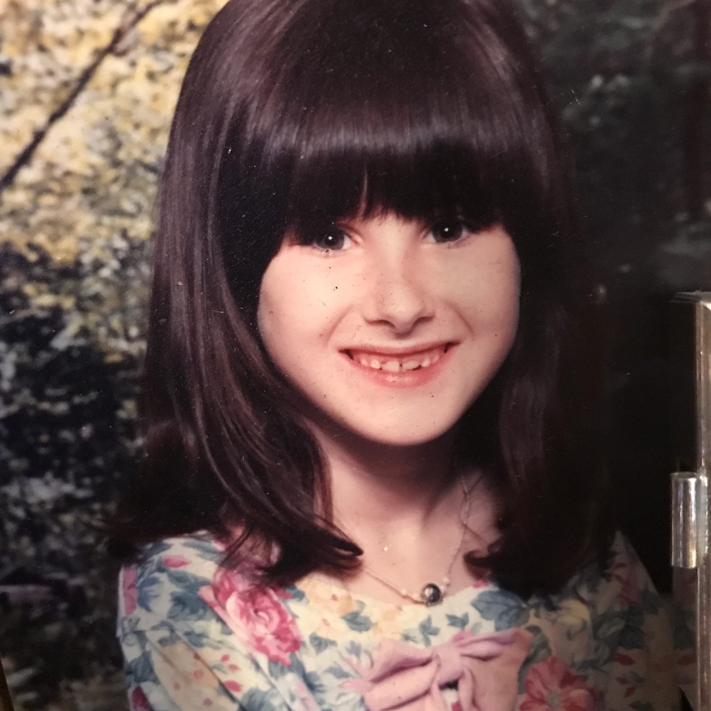 Young Lyric, smiling as required for a photo. They have black hair, a pale face, and newly growing in front teeth.