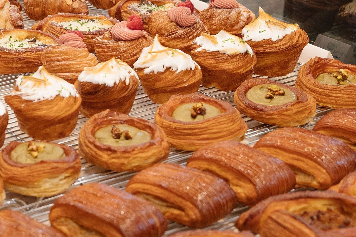 Rows of croissants, kouign amann, and more on a bakery countertop