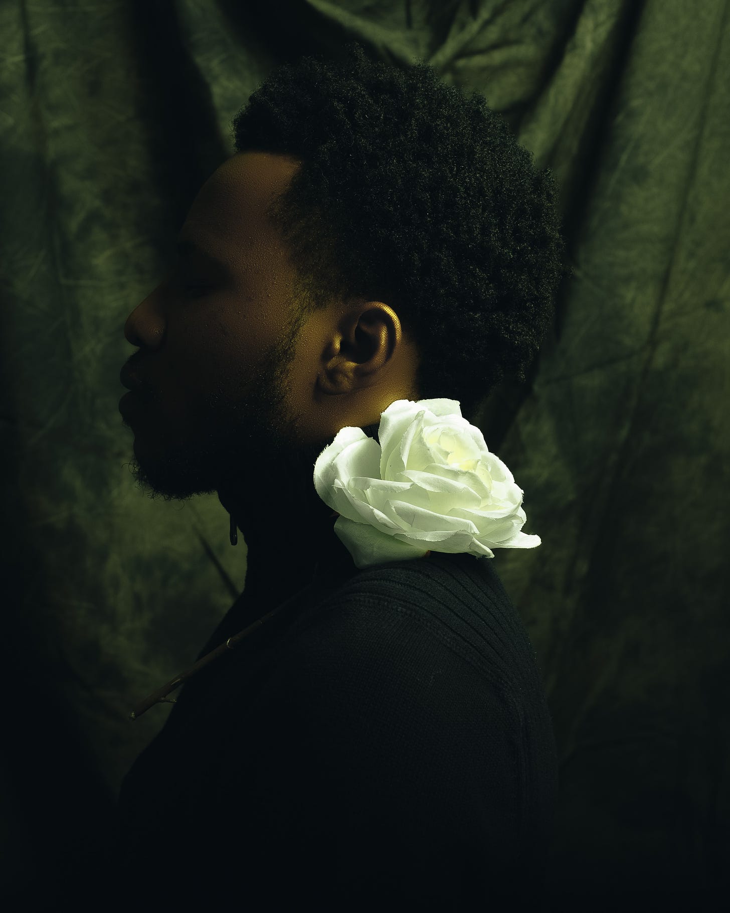 black man facing sideways with a white rose on his shoulder