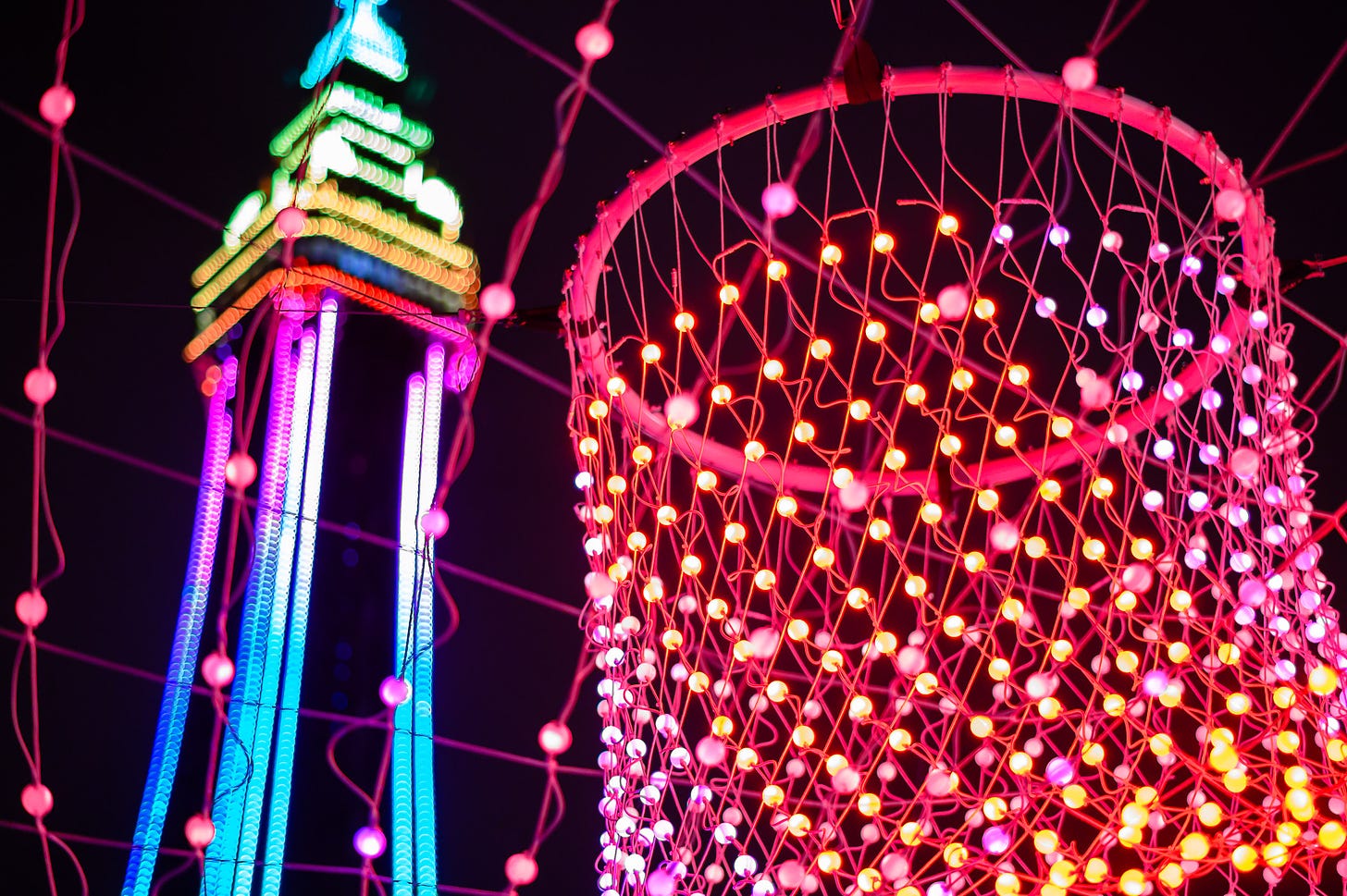 A net of LED lights in front of Blackpool Tower which is lit up with rainbow colours.