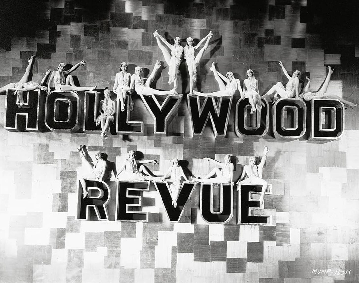 Title card for The Hollywood Revue of 1929, featuring dancers posed on top of giant letters spelling out "HOLLYWOOD REVUE"