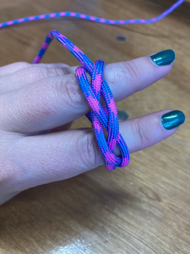 A woggle in progress - a length of bright blue and pink paracord wrapped around my fingers as I start to weave it into a Turk's Head Knot.