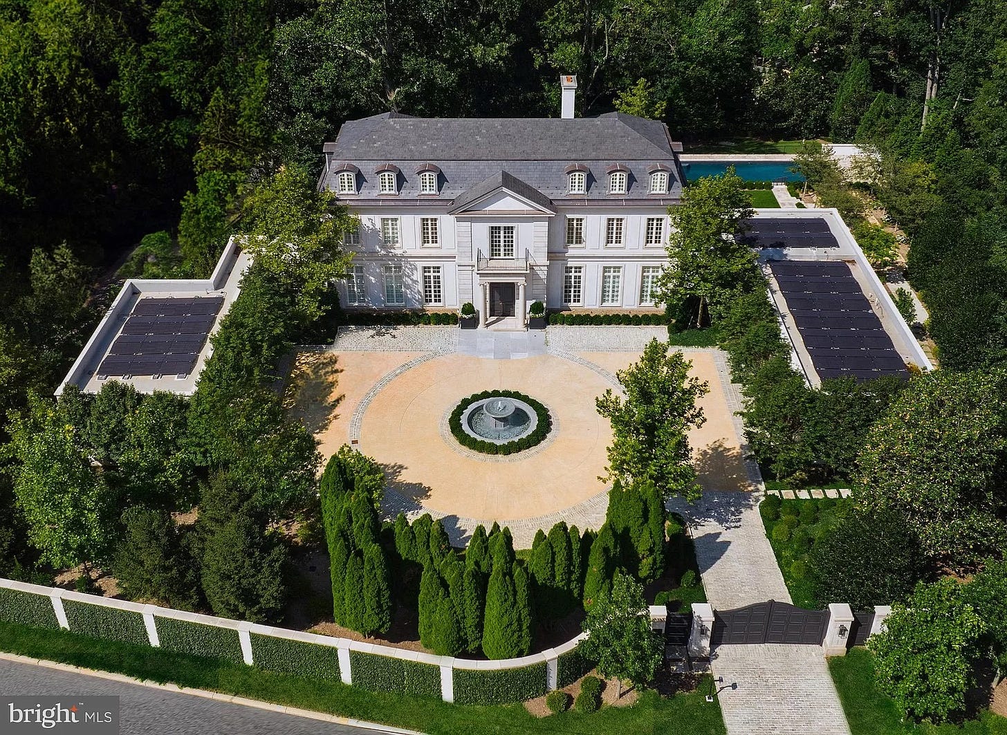 Aerial view of a large mansion with solar panels on two adjacent flat roofed structures — garages we guess.