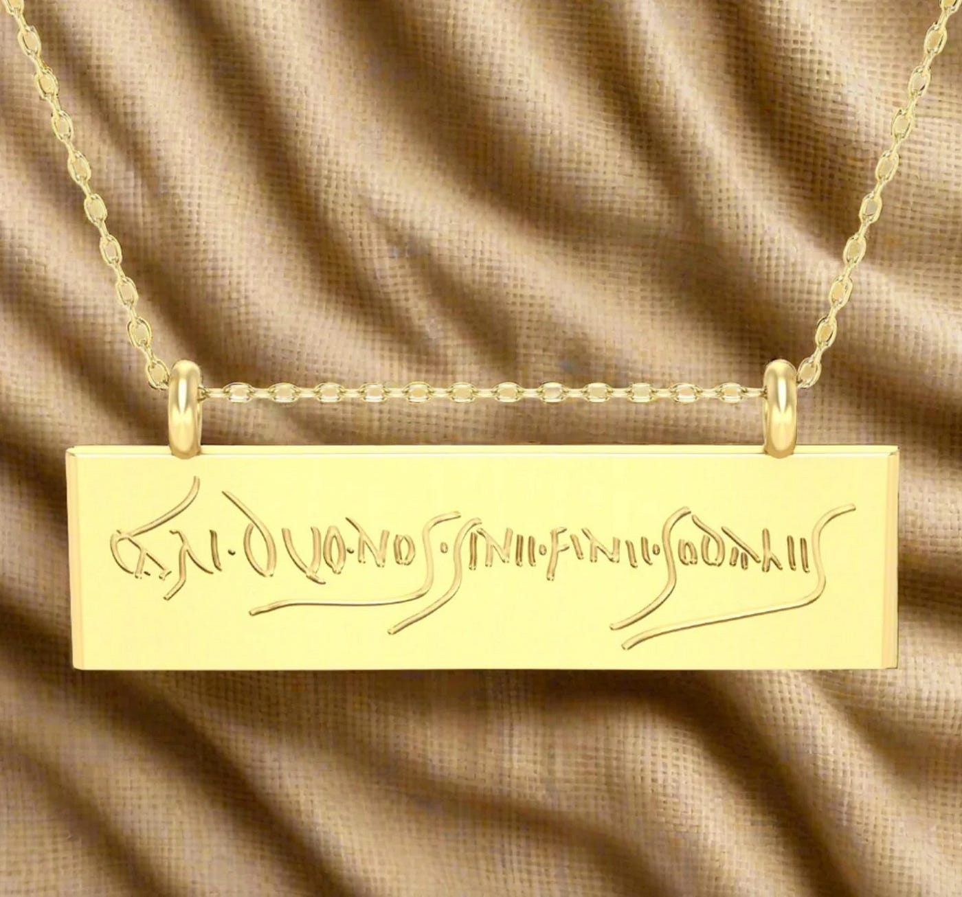 A gold chain with a horizontal rectangular pendant that has Latin graffiti on it