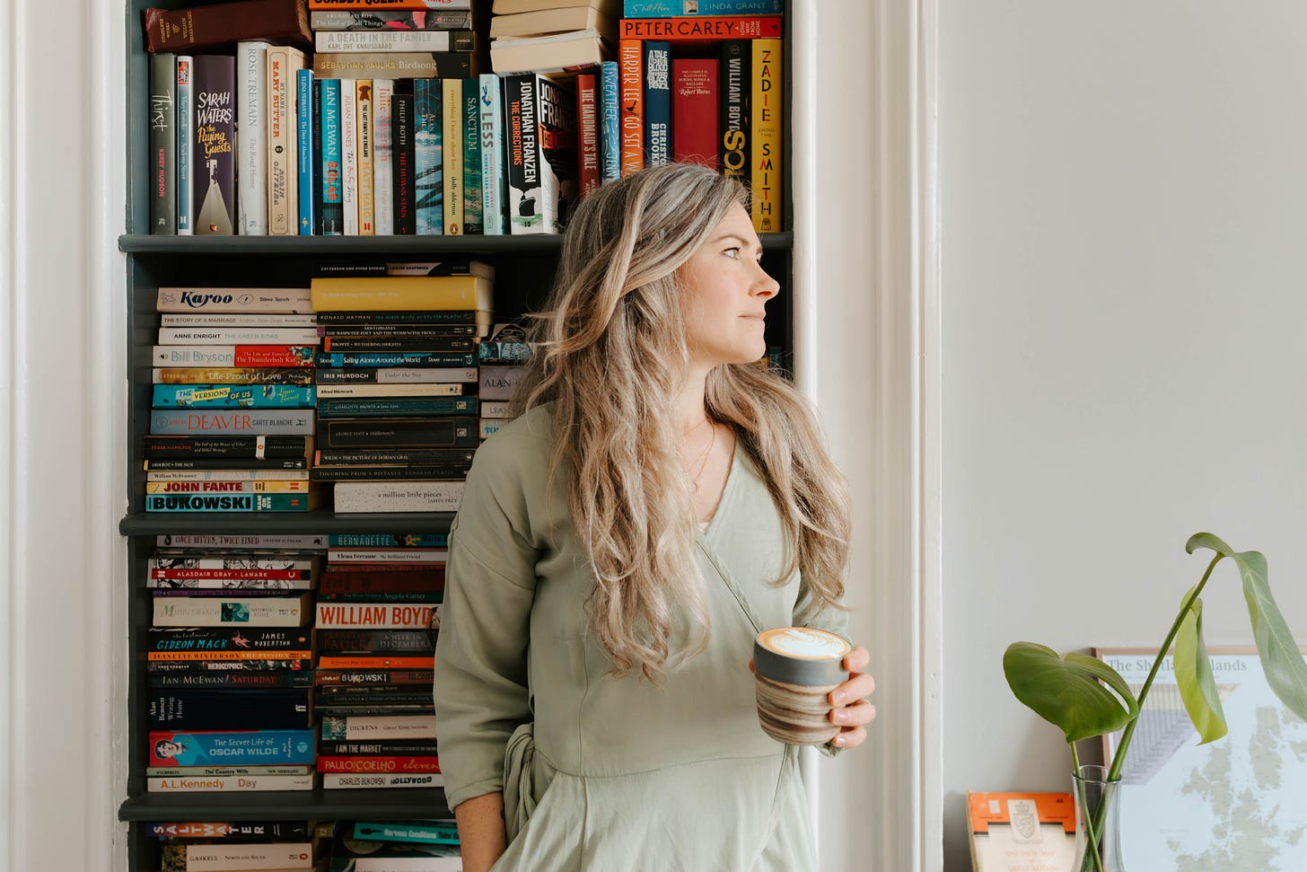 white woman stands in front of a bookcase holding a coffee