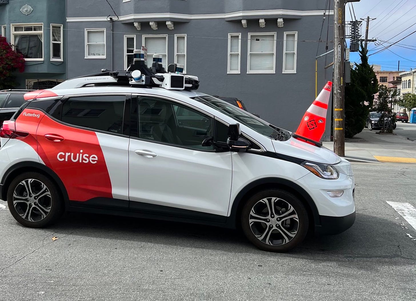 A driverless Cruise car stopped by a traffic cone on its hood.