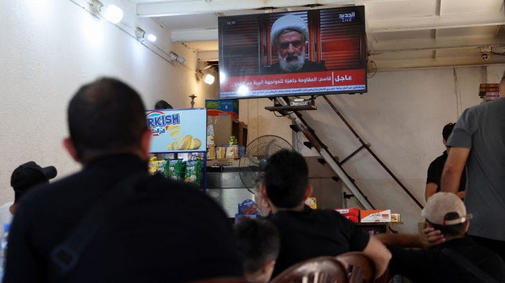 People watch Hezbollah deputy leader Sheikh Naim Qassem delivering a televised address