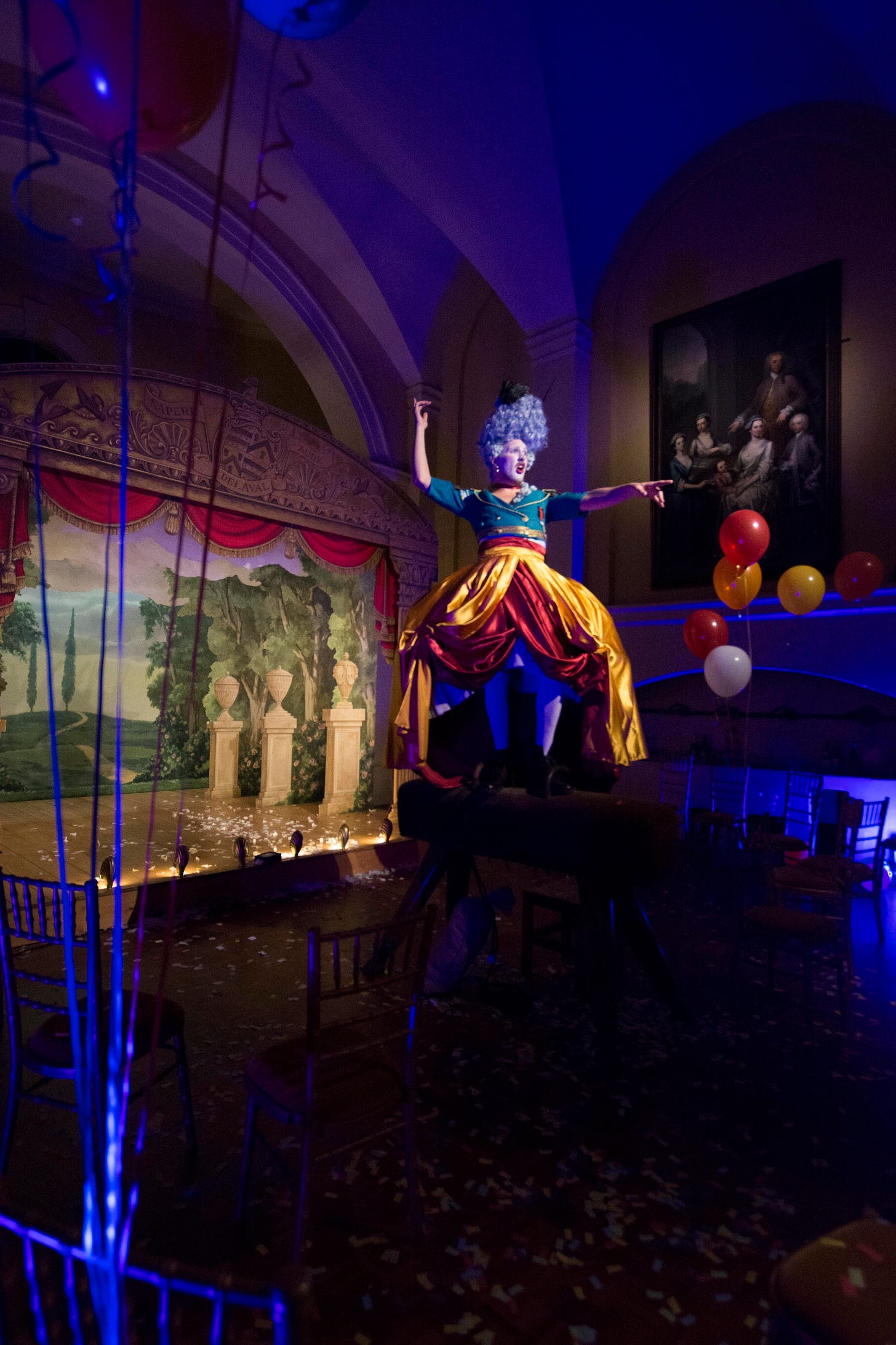Georgian drag artist stands on top of a pummel horse with a theatre back drop and balloons