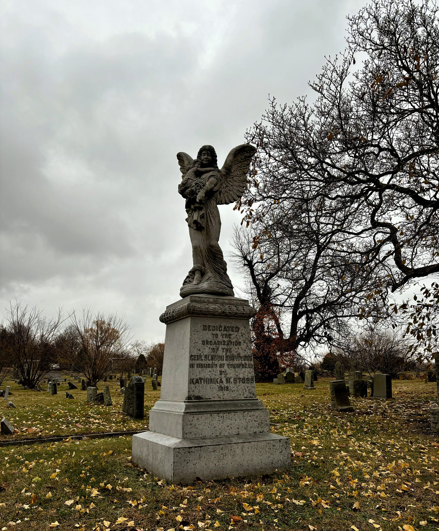 An angel holds a child in its arms and points down to the ground. The base reads: Dedicated to the Organization of the Genl Slocum Survivors in Memory of Their Dead by Kathinka M. Stoss 1912.