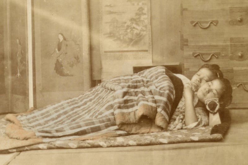 old photo of two geisha sleeping on the floor with blankets and takamakura