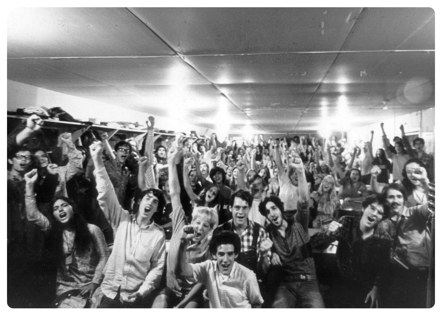 A black & white photo from the 1960's, found under google image search results 'Free Love' shows nearly 100 young people in a room cheering